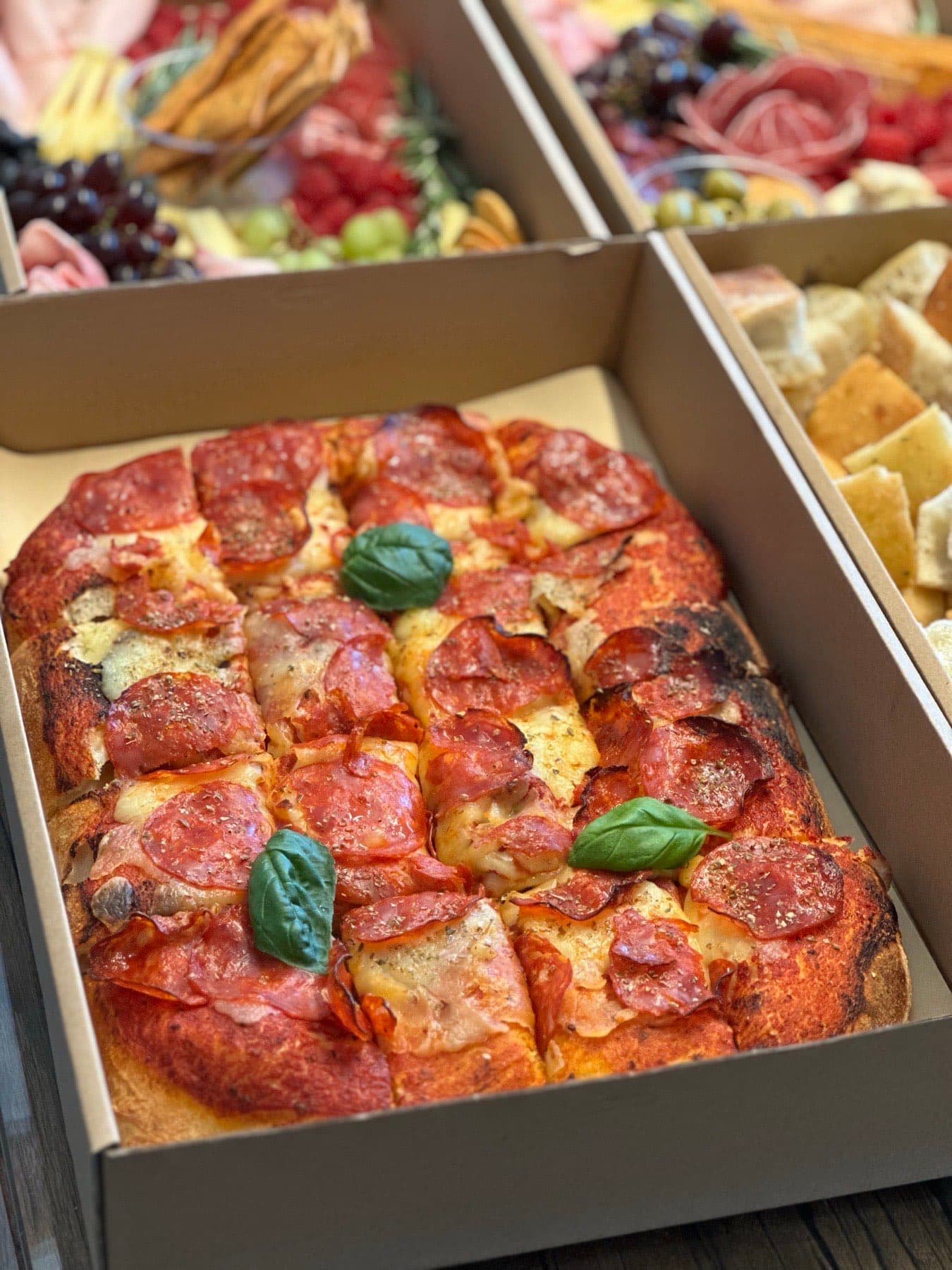 Blechpizza mit Salami und Basilikum auf Kartonblech